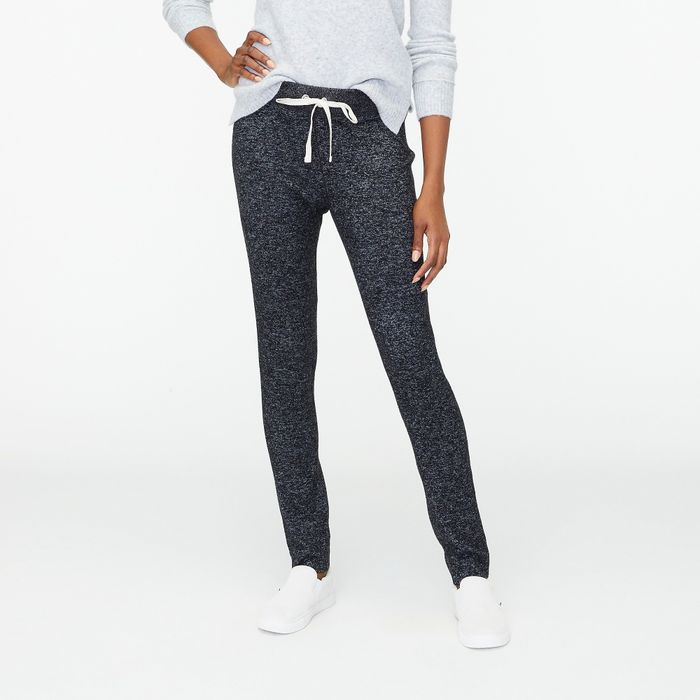 A model dressed in dark grey sweatpants, a light grey top, and white sneakers