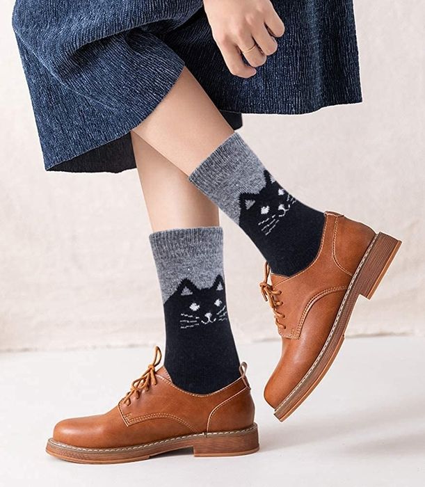 A model wearing grey socks adorned with black cat faces peeking out from a pair of Oxfords.