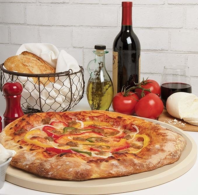 The large round stone with a freshly made pizza on top.