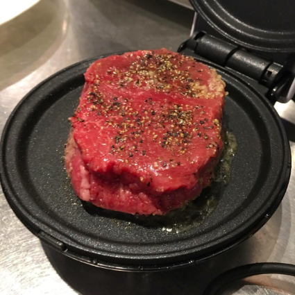 A raw piece of meat sizzling on the griddle.