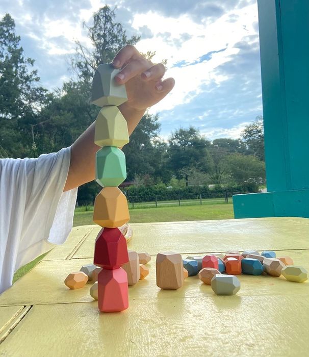 A child stacking colorful, geometric wooden blocks outside on a sunny day.