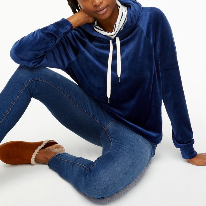A model showcasing a blue velour hoodie, paired with jeans and cozy brown fuzzy slippers