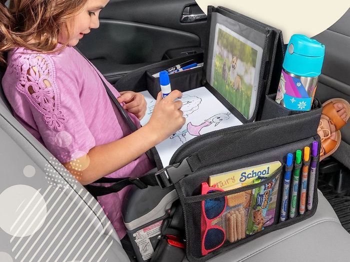 Child sitting in a car, drawing with a black travel tray on their lap