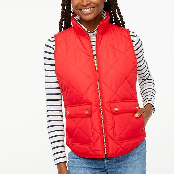 A model sporting a red puffer vest layered over a striped tee and paired with jeans