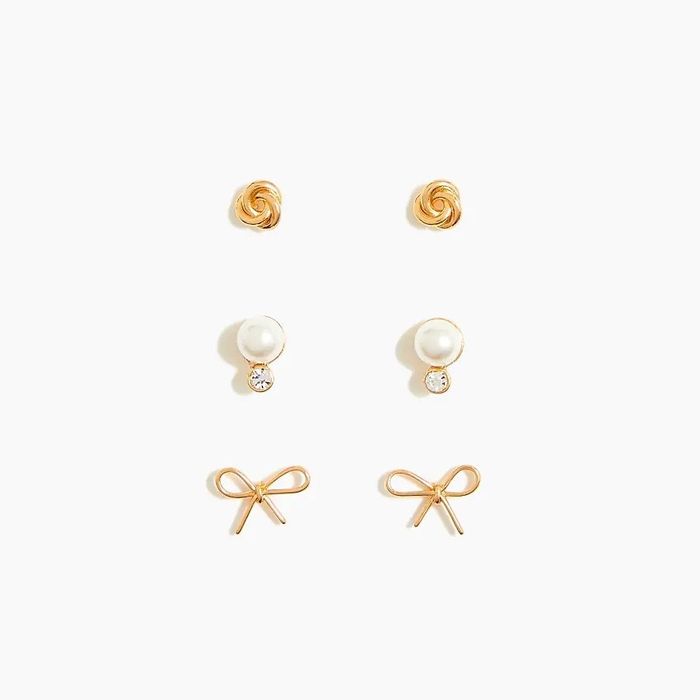 Three pairs of gold earrings featuring a bow design, a pearl and diamond set, and a gold swirl pattern