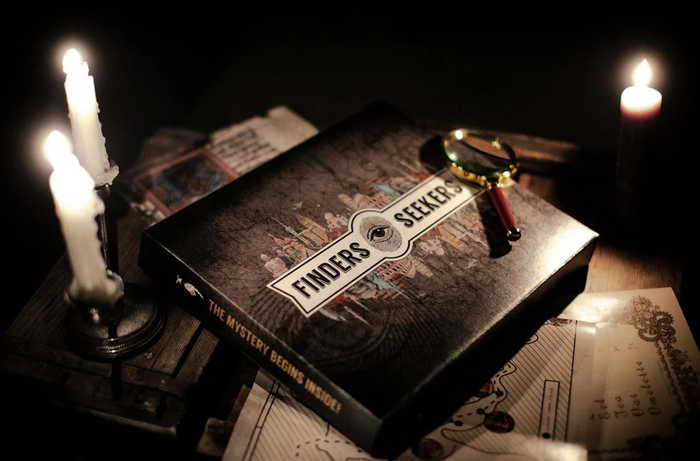 Finders Seekers board game set with candles and a magnifying glass on a dark table, creating a mysterious and intriguing atmosphere