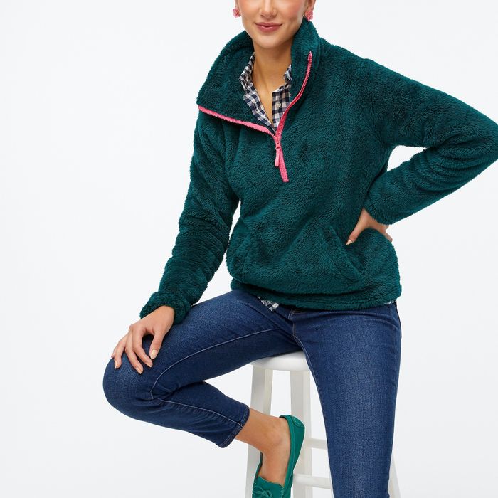 A model sporting a green half-zip sweater, styled with jeans and a blue-and-white top