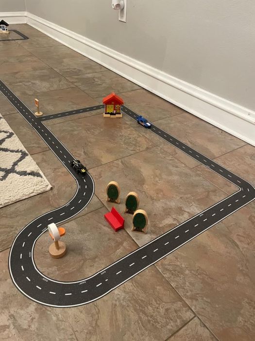 A toy road set spread across the floor with tiny buildings and trees; features a winding track and toy vehicles, ideal for creative play.