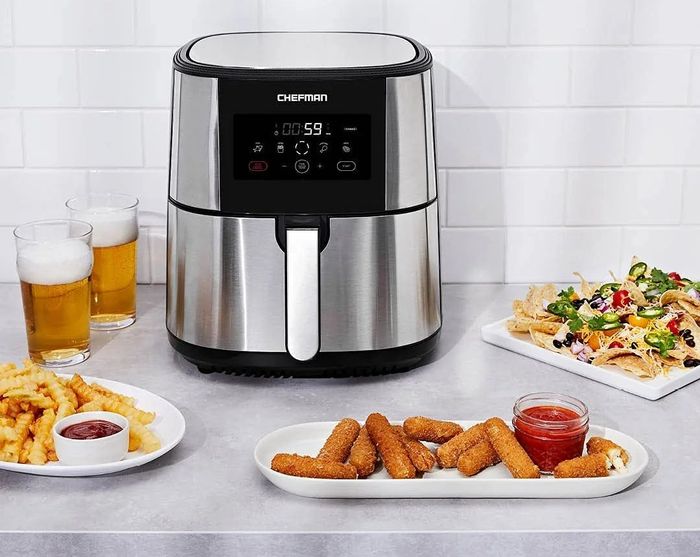 An air fryer sitting on a countertop with fries, mozzarella sticks, nachos, and beer, accompanied by the text 'Healthy Fried Favorites.'