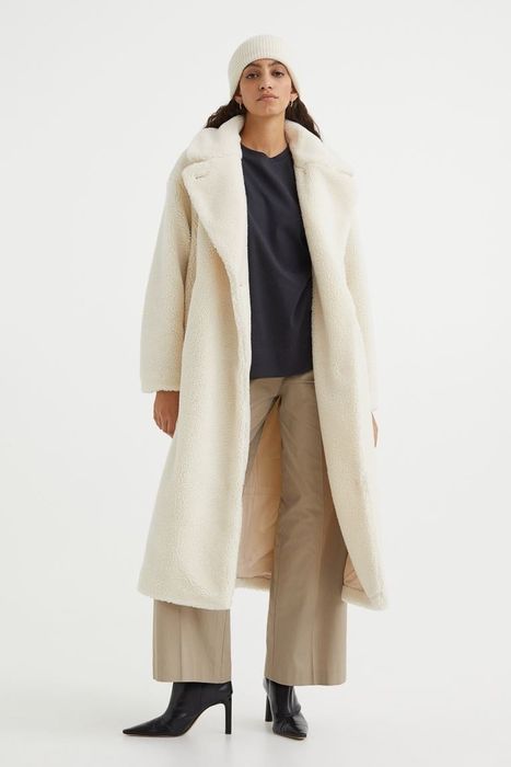Model styling a shin-length teddy bear fleece coat in a soft cream hue