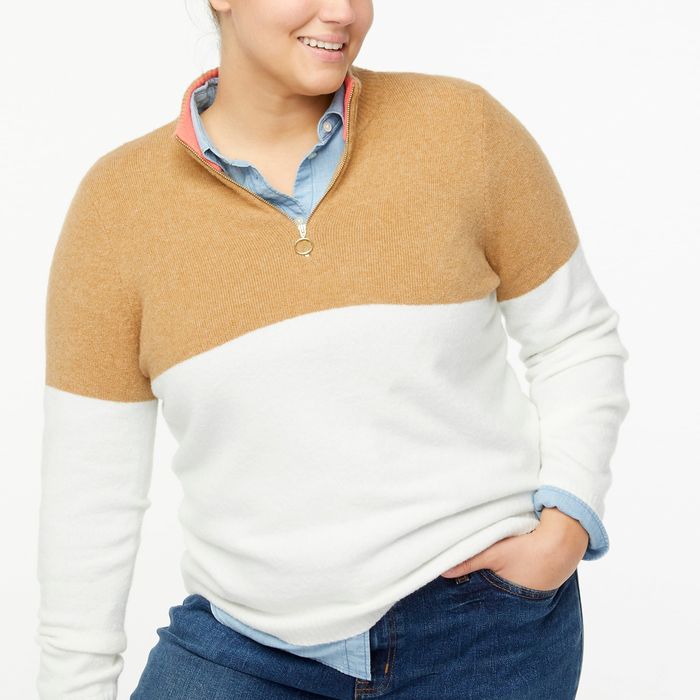 A model dressed in a tan and white quarter zip, paired with a blue shirt and jeans