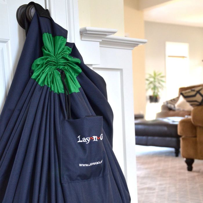 A hammock chair suspended indoors near a sofa and plant, with a visible storage pocket showing a brand logo