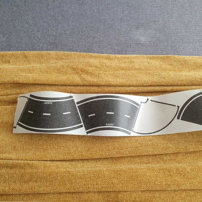 A strip of adhesive road decals laid out on a textured surface, showing various curving street designs, perfect for children playing with toy cars.