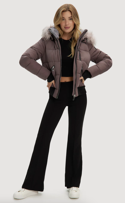 A model donning a short plum puffer bomber jacket featuring a vegan fur-lined hood