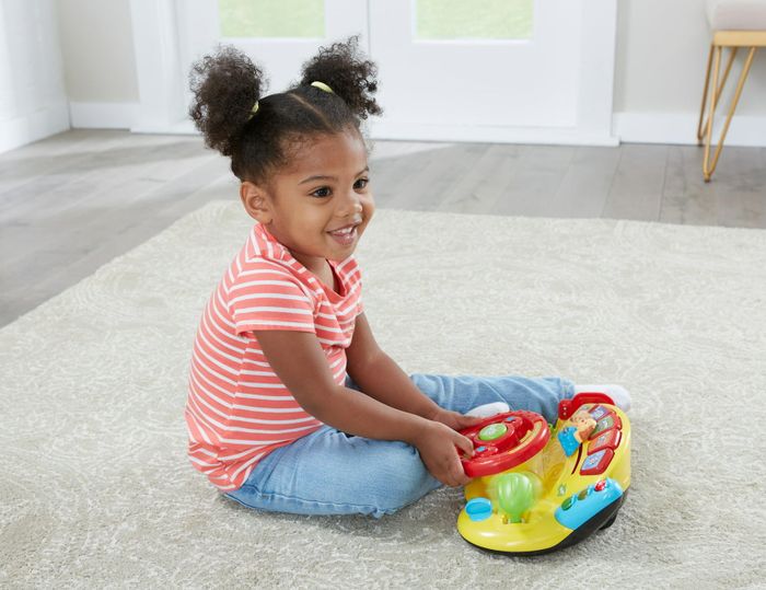 A girl enjoying playtime with a toy steering column.