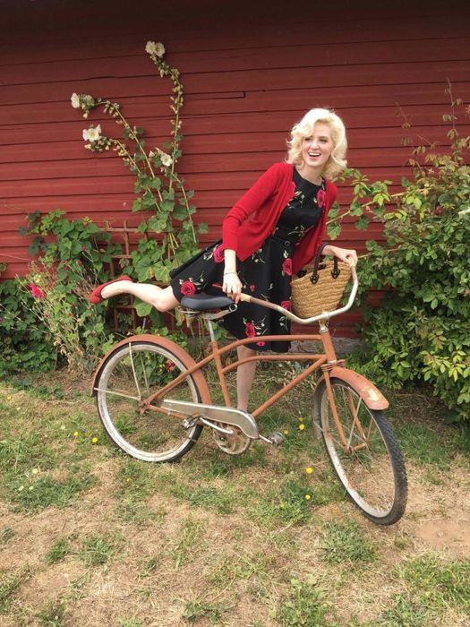 A reviewer is shown in a black dress adorned with red florals, complemented by a red cardigan.