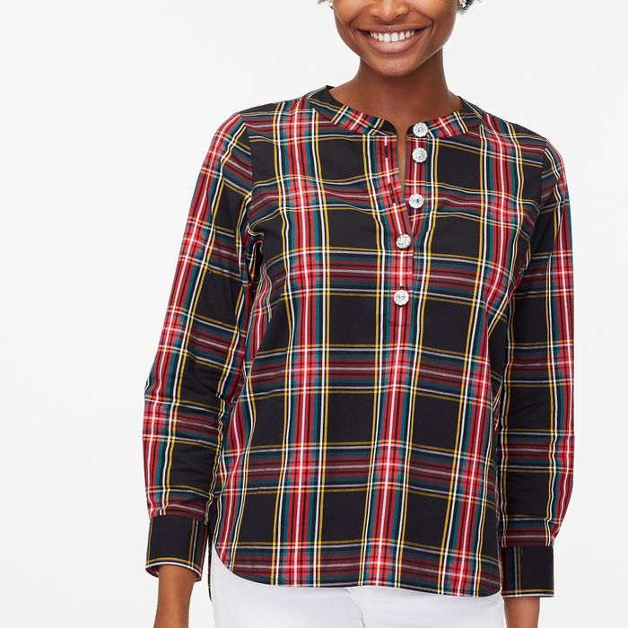 A model styled in a red, black, gold, and blue plaid top featuring gemstone buttons, paired with white pants