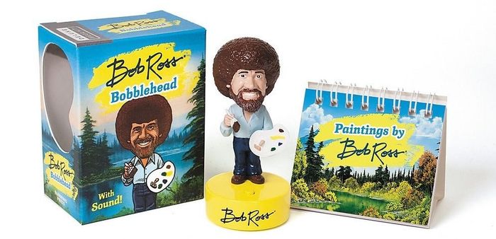 The bobblehead alongside a mini book featuring Bob Ross's artwork