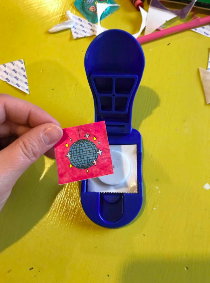 A hand assembling a sticker by placing a paper design over a puffy circle and attaching the sticker back in the small press.