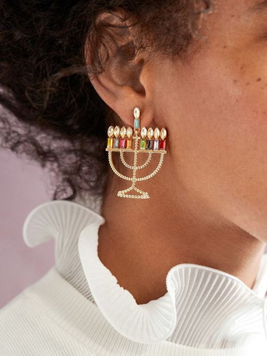 A model flaunting the gold menorah earrings adorned with colorful, jewel-like candles.