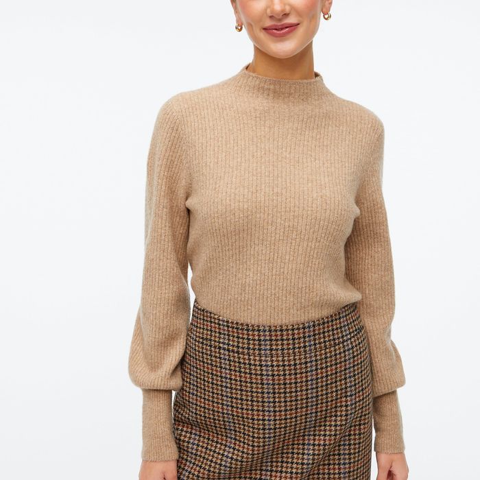 A model showcasing a tan mock neck sweater paired with a tan, red, and black skirt