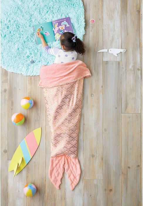 A child wrapped in a sparkly pink blanket that gives the illusion of a mermaid tail.