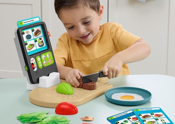 A child playing with a toy cooking set, chopping plastic food on a cutting board with a play tablet in the background. Text highlights fun learning for children aged 3 and up.