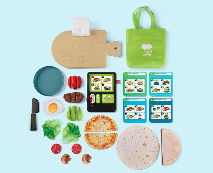 A toy cooking set featuring a play tablet, recipe cards, and over 20 food pieces and tools, including pita, pizza, and various vegetables.