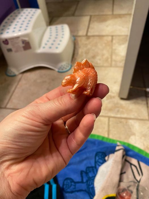 A hand holding a small plastic dinosaur toy in a bathroom setting.