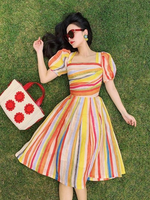 A model relaxing in the grass while wearing a rainbow-hued puff sleeve square neck midi dress.