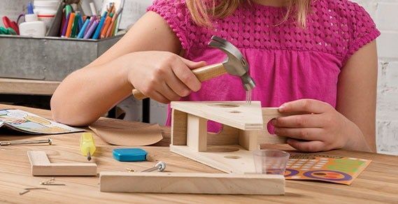 a young child hammering a nail into wood