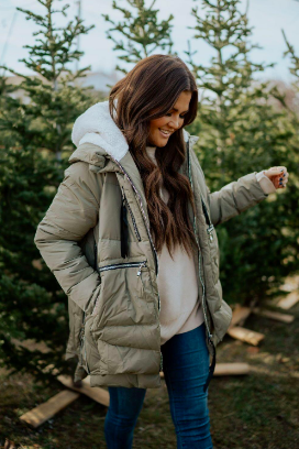 A reviewer sporting the coat with a hoodie underneath, featuring zipper front pockets, side pockets, a fluffy hood, and a plush texture.