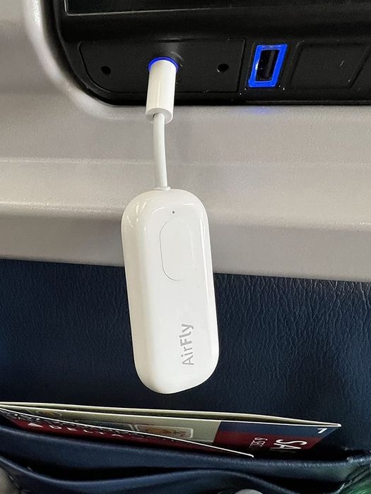 Reviewer image showing the AirFly Pro plugged into the headphone jack at the back of a plane seat
