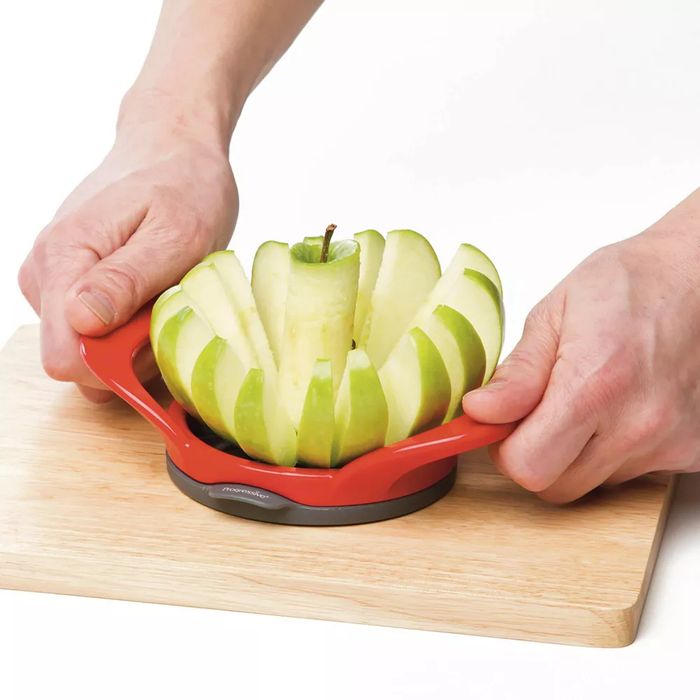 Someone cutting an apple with a slicer on a wooden chopping board