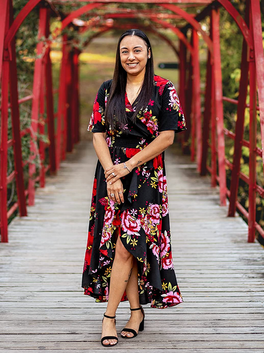 A reviewer is seen wearing a black maxi wrap dress adorned with red and pink flowers.