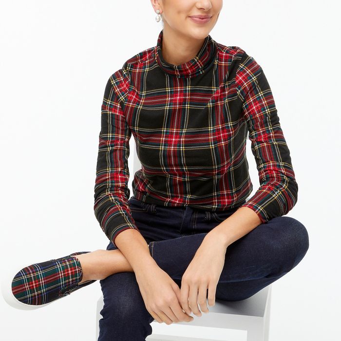 A model wearing a red, green, black, and white plaid turtleneck paired with jeans and matching shoes