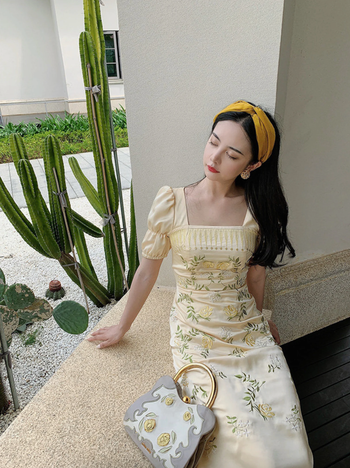 A model lounging in a yellow dress adorned with yellow embroidered flowers