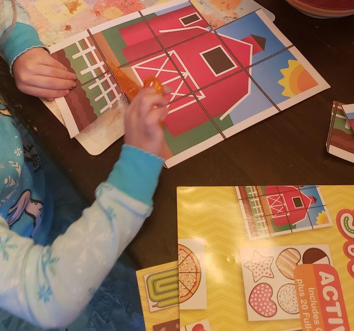A child using the scissors to cut out a farmhouse image from the activity pad