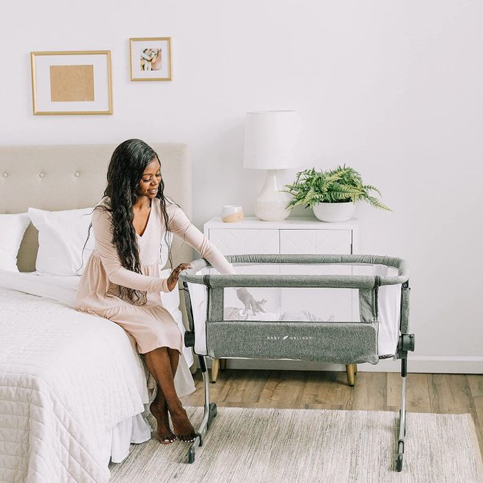 A parent sitting up in bed, next to a bedside bassinet.