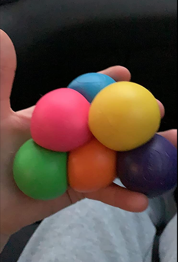 Reviewer holding six squishy balls in various rainbow colors in their hand