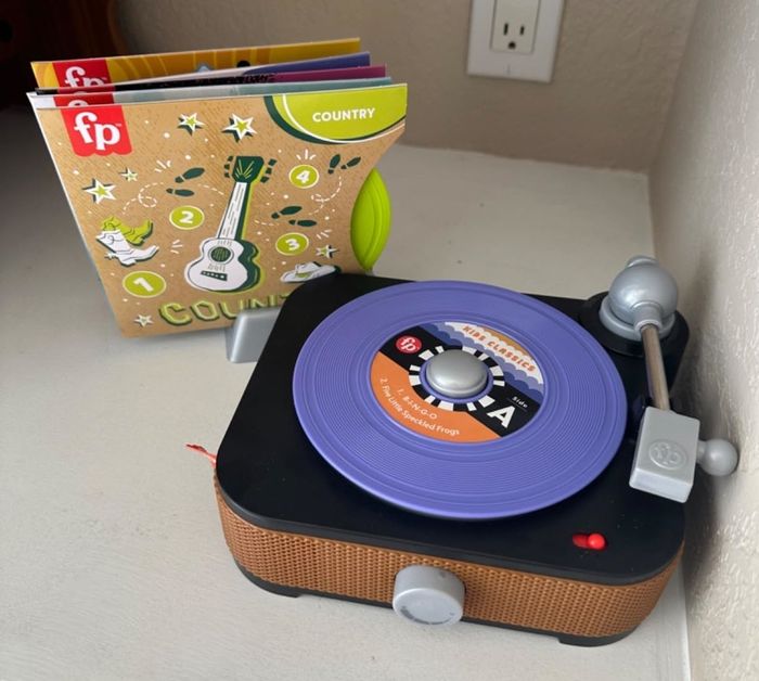 Toy record player with a stack of plastic records beside it. Album cover labeled
