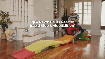 A child model happily riding a red scooter down a colorful ramp.