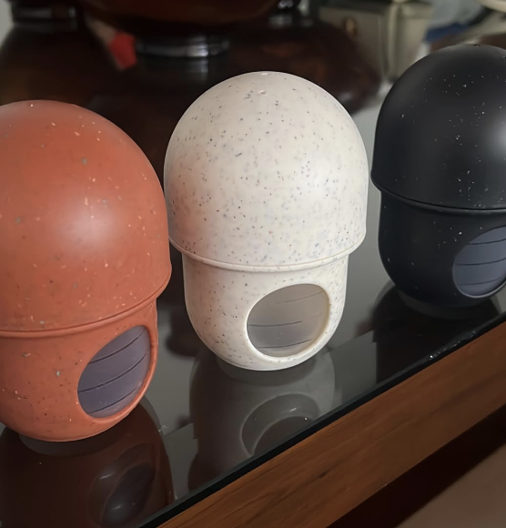 Three dome-shaped spice jars with clear circular windows are arranged on a glass shelf. The jars are in red, white, and black colors.