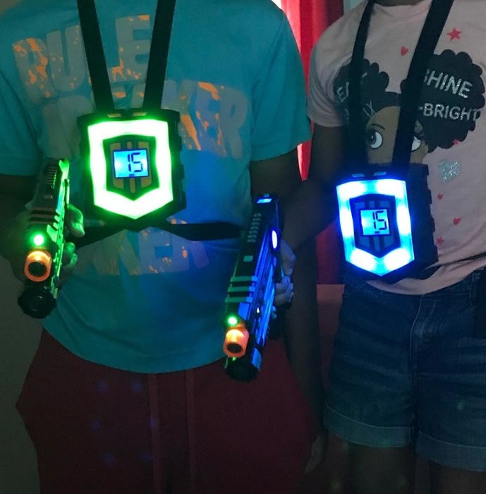 A reviewer's photo showing two people in glowing vests, each holding a lit laser gun