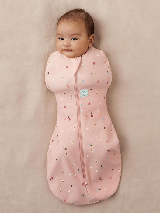 A baby in a pink zip-up swaddle, resting on a neutral-colored background, featured in a shopping guide.