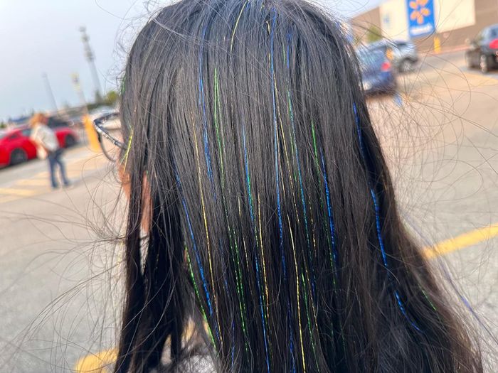 A reviewer’s child showing off their hair with blue and gold sparkly tinsel strands