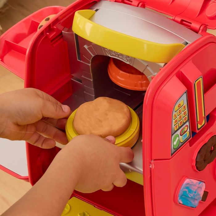 A child's hands using a toy oven to mold and bake pretend food from dough.