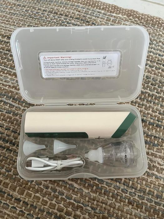 An ear cleaning kit that includes an ear vacuum cleaner, various nozzles, and a USB charging cable, all neatly stored in a plastic case on a woven surface.