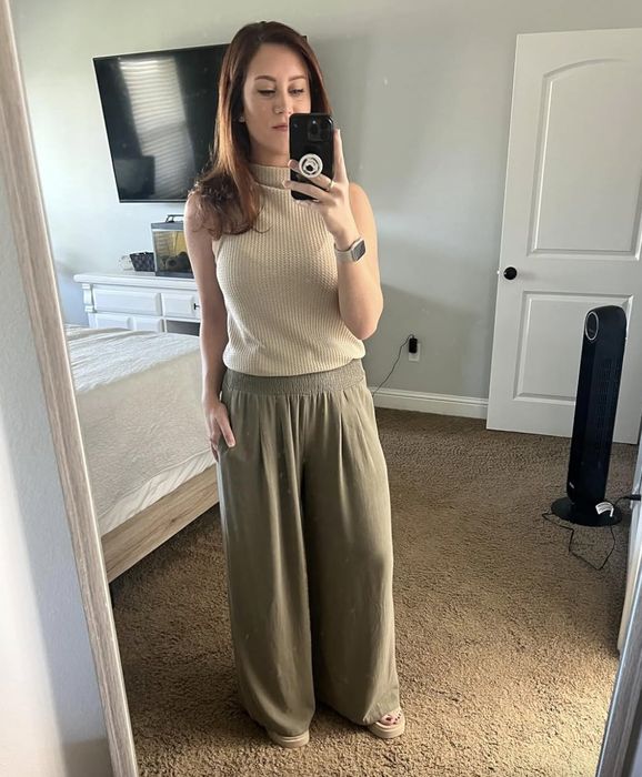 A person snaps a mirror selfie while wearing a sleeveless top and wide-legged pants.