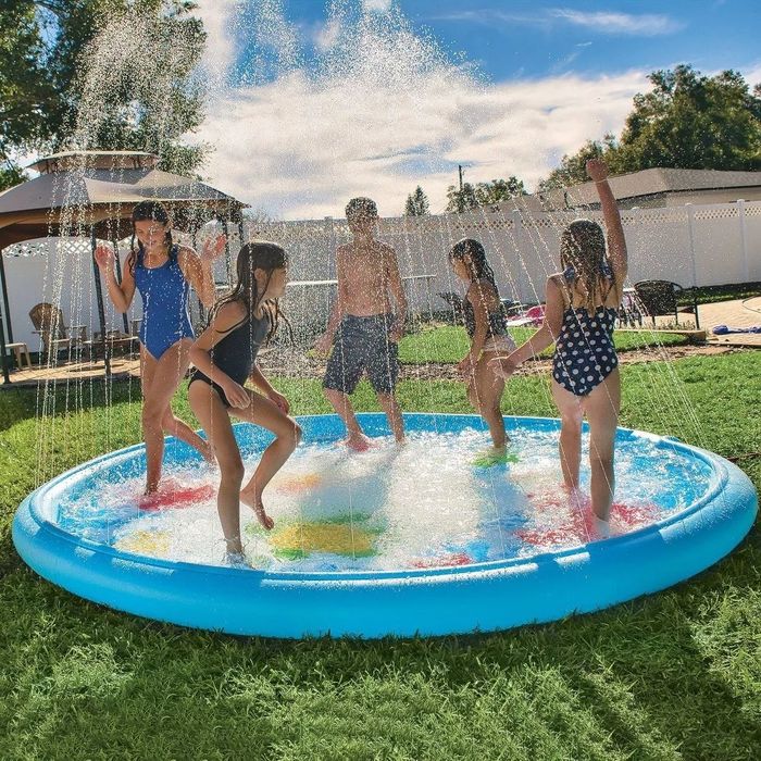 Children of different ages having fun on the splash pad in the grassy yard